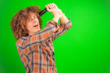 Ele avuca sığmayan bukleli çocuk saçını budayarak günlük bir gömlek giyer. Saf yeşil renkli anahtar arka plan çekici ve profesyonel imaja çok yönlülük ve canlılık katar.