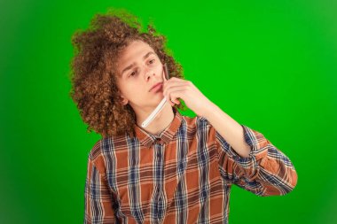 Kıvırcık saçlı çocuk, kıtır kıtır bir gömlek giyip yüzünü ustura ile dikkatlice tıraş eder. Canlı yeşil krom anahtar, görüntünün temiz ve profesyonel estetiğini güçlendirir.