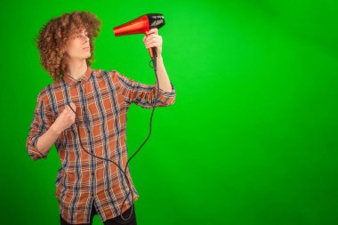 Işıl ışıl, kıvırcık saçlı genç adam yeşil ekranda kendine saç kurutma makinesi doğrultuyor.