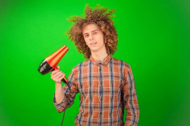 Genç adam elinde saç kurutma makinesiyle Chroma Key sahnesini kucaklarken neşeli bir esinti buklelerinden ve gömleğinden eser.