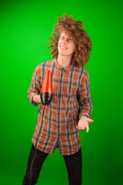 Kıvırcık saçlı adam, Chroma Key 'in yemyeşil arka planına karşı elbisesinde akış hareketi yaratmak için bir saç kurutma makinesi kullanıyor.