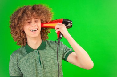 Chroma Key ekranı kıvırcık saçlı adamın neşeli enerjisini çerçeveler, gömleği bir saç kurutma makinesinin kontrollü rüzgarı altında dalgalanır.