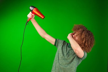 Kıvırcık saçlı bireyin saç kurutma makinesi, gömleği ve saçı zarif bir şekilde Chroma Key setinde hareket ederken dinamik bir sahne ortaya çıkıyor.