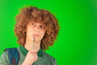 İlham veren kıvırcık saçlı genç adam parlak yeşil Chroma Key ekranına karşı parlak bir defter tutuyor, odak ve profesyonellik yayıyor.