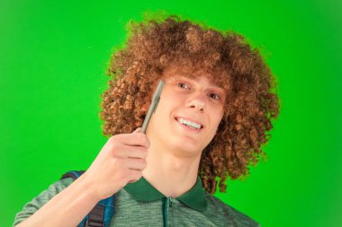 Yaratıcılığını ön plana çıkaran kıvırcık saçlı genç adam elinde bir defterle Chroma Key yeşiline karşı parlak bir şekilde poz veriyor.