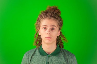 Sınırsız şaşkınlıkla tepki veren kıvırcık saçlı genç adam parlak yeşil Chroma Key arka planına karşı gözleri açık duruyor.
