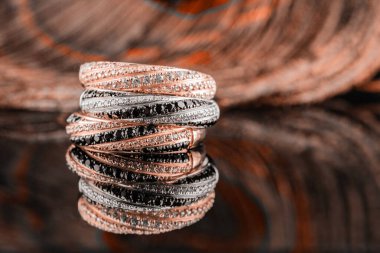 Alyanslar aynaya yansıyor. Tavus kuşu tüylerinin arka planında üç halka. Siyah ve beyaz taşlı altın ve gümüş yüzükler.