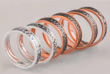 Üç metalden yapılmış alyanslar. Beyaz arkaplanda altı halka var. Yüzeyi pürüzlü altın ve gümüş halkalar.