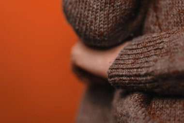 Mor örgü kazaklı bir kadın elini dirseğinin altına koydu, yüzünü göstermeden, yakın çekim. Yakınlık ve belirsizlik belirtisi. Sözsüz işaret dili, yatay resim