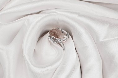 Moda aksesuar altın yüzük. Arkaplanı taştan. Beyaz saten arka planında büyük bir ametist bulunan klasik gümüş bir yüzük. Büyük pembe taşlı bir yüzük.