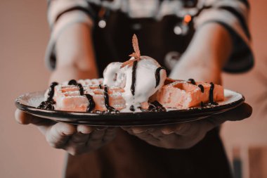 Ellerinde waffle tutan kız. Dondurma ile servis edilir. Çay saati için lezzetli bir tatlı. Yemek pişirme süreci. Tatlı ikram ediyorum. Muzlu, dondurmalı ve çikolatalı Belçika waffleları. Tatlı waffle 'lar