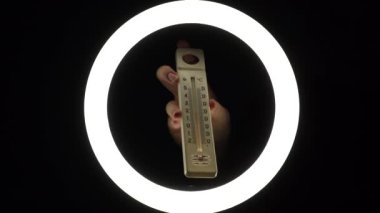 plastic alcohol thermometer with a red stripe in female hands close-up on a black background. temperature measurement concept.