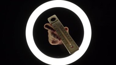 plastic alcohol thermometer with a red stripe in female hands close-up on a black background. temperature measurement concept.