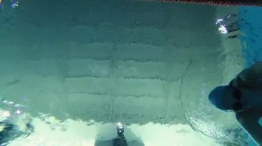Eşofmanlı, dalış gözlüklü, mayo takan kadın yüzücü havuzda antrenman yapıyor. Sporcu su altında yüzer. Sualtı çekimi, geniş açı, 4K.