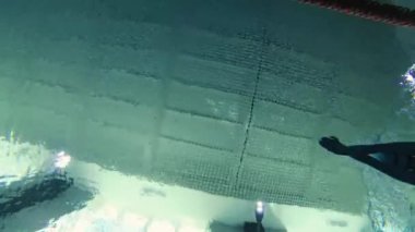 Eşofmanlı, dalış gözlüklü, mayo takan kadın yüzücü havuzda antrenman yapıyor. Sporcu su altında yüzer. Sualtı çekimi, geniş açı, 4K.