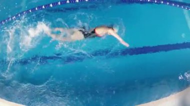 Eşofmanlı, dalış gözlüklü, mayo takan kadın yüzücü havuzda antrenman yapıyor. Sporcu serbest bir şekilde yüzer. Geniş açı, 4k..