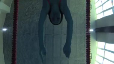 Eşofmanlı, dalış gözlüklü, mayo takan kadın yüzücü havuzda antrenman yapıyor. Sporcu su altında yüzer. Sualtı çekimi, geniş açı, 4K.