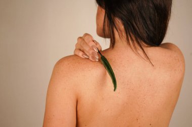 Siyah saçlı bir kız nazikçe sırtını küçük bir tüyle okşar. Onun çıplak sırtı doğal güzelliği ve kadınlığı ön plana çıkarıyor. Bej rengi pastel duvar resme yumuşaklık ve zarafet katar.