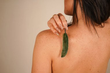 Siyah saçlı bir kız nazikçe sırtını küçük bir tüyle okşar. Onun çıplak sırtı doğal güzelliği ve kadınlığı ön plana çıkarıyor. Bej rengi pastel duvar resme yumuşaklık ve zarafet katar.