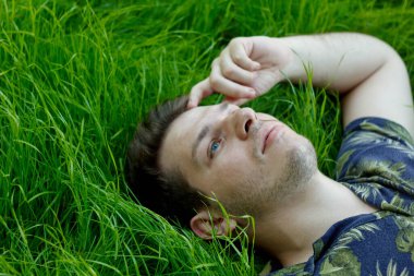 Yeşil çimenlerde yatan bir adamın yakın plan fotoğrafı. Doğadaki huzurlu an, bir rahatlama ve çevreyle uyum hissini yakalar. Huzurlu ortam, sakin atmosferi arttırır.