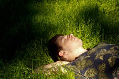 Yeşil çimenlerde yatan bir adamın yakın plan fotoğrafı. Doğadaki huzurlu an, bir rahatlama ve çevreyle uyum hissini yakalar. Huzurlu ortam, sakin atmosferi arttırır.