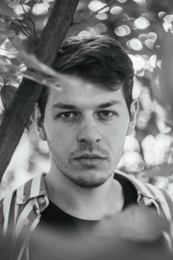 Orman zeminine karşı bir adamın yüzünün çarpıcı siyah beyaz görüntüsü. Sahne güçlü bir birlik duygusu ve paylaşılan enerjiyi yansıtıyor. Doğayla olan bağlantının görsel bir ifadesidir.