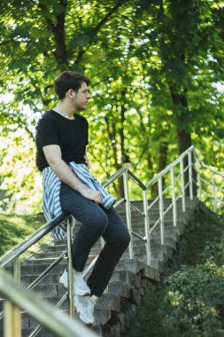 Sitting on the street stair railing, a young man waits for a date. The serene surroundings create a romantic atmosphere. His quiet wait adds to the calm yet excited feeling clipart