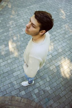 Yüksek bir bakış açısından, bir adam kaldırım taşlı bir caddede duruyor. Bakış açısı, kentin hareketli ortamındaki konumunu vurguluyor. Şehir manzarası ana derinlik katıyor.