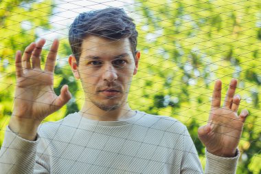 Haşin bir ifadeyle genç bir adam örgüden dışarı bakar. Bakışlarının ciddiyeti derin bir tefekkür hissi veriyor. Onun özellikleri yoğun duyguların özünü yakalar.