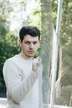 Beyaz bir kazak giyen bir adam, bir ağı eliyle kavrıyor, düşüncelere dalmış. Dalgın duruşu önemli bir şeyi yansıttığını gösteriyor. Görüntü sakinliği ve sessizliği çağrıştırıyor.