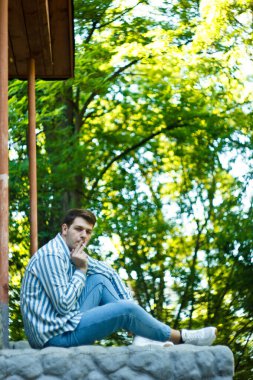 Kaldırımda oturan bir adam, düşüncelere dalmış bir şekilde sigara içiyor. Anın durgunluğu onun içsel ruh halini vurguluyor. Kompozisyon sükuneti ve sessizliği yansıtıyor.