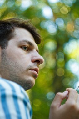 Elinde sigara tutan, nefes veren bir adamın yakın çekimi. Kibar bukleler sahneye sükunet ve sessizlik katıyor. İçine kapanık ifadesi sakinlik atmosferini arttırıyor.