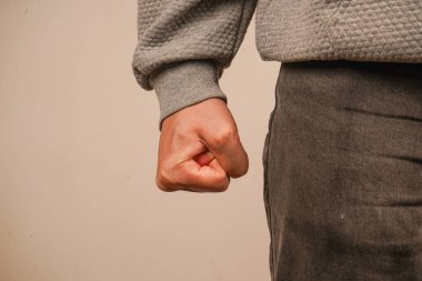 Bir adam elini sıkıca yumruğa sıkıca tutar, bütün tendonlar ve damarlar görünür. Işık duvarının arka planında, bir el yumruğa sıkıştı.