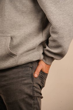 Bir adam elleri kotunun arka cebinde durur. Onun basit kıyafeti rahatlık ve güven duygusunu vurguluyor. Duruşu sakin ve rahat olduğunu gösteriyor.