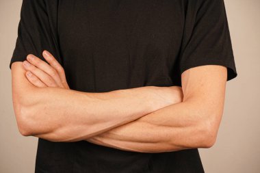 Bir adam kollarını koruyucu bir pozda kavuşturur, elleri göğsünün yanında birbirine yaslanır. Yakın çerçeve, kendi yansımasını ya da savunmasızlığını yakalar. Ayarların basitliği vücut dilini güçlendirir.