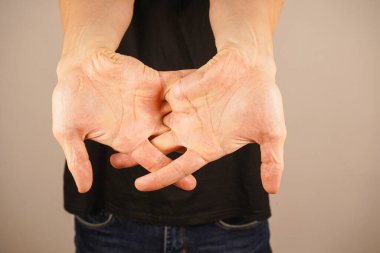 Hands locked behind the back against the background of a black T-shirt. A man's hands are intertwined behind his back clipart