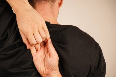 Hands locked behind the back against the background of a black T-shirt. A man's hands are intertwined behind his back clipart