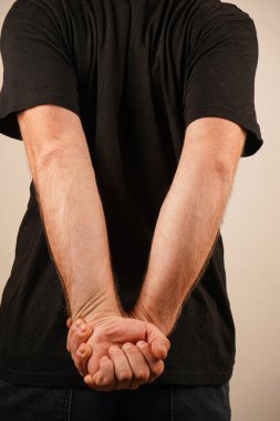 A young man in a black T-shirt. The man holds his hands behind his back, as if doing a warm-up. His hands are clasped with their palms together clipart