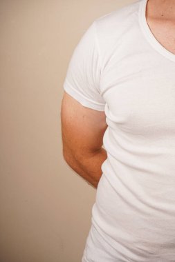 Düz beyaz tişört giyen bir adam, belden yukarısına çekilmiş. Basit kıyafet onun rahat ve rahat tarzını ön plana çıkarıyor. Tarafsız arka plan, temiz tasarıma odaklanmamızı sağlar.