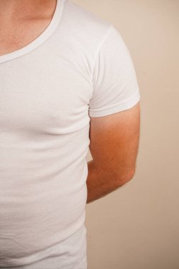 Düz beyaz tişört giyen bir adam, belden yukarısına çekilmiş. Basit kıyafet onun rahat ve rahat tarzını ön plana çıkarıyor. Tarafsız arka plan, temiz tasarıma odaklanmamızı sağlar.
