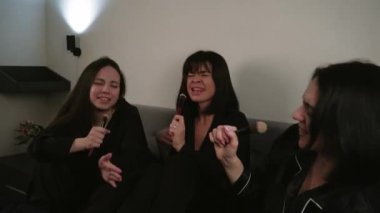 Kızların mikrofonla doğaçlama yaptığı ve kanepede beyaz bir duvara karşı dans etmekten zevk aldığı eğlenceli bir karaoke partisi.