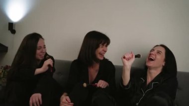 Kızların mikrofonla doğaçlama yaptığı ve kanepede beyaz bir duvara karşı dans etmekten zevk aldığı eğlenceli bir karaoke partisi.