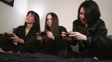 Dost canlısı atmosfer: üç siyah pijamalı kadın aydınlık bir duvara karşı dizüstü bilgisayar oyunları oynuyorlar.