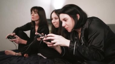 Dost canlısı atmosfer: üç siyah pijamalı kadın aydınlık bir duvara karşı dizüstü bilgisayar oyunları oynuyorlar.