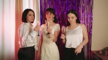 Gelin beyaz gelinliğiyle parıldıyor, arkadaşlarıyla bekarlığa veda partisini kutluyor, pembe arkaplanlı pullarla.