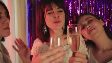 Klasik beyaz bir gelinlik giyen müstakbel gelin, bekarlığa veda partisini bir bardak şampanyayla kutluyor. Arka planda mor parlak kurdeleler