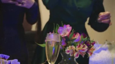 Kadınlar arka planda parıltılı ve parlak kurdeleli aydınlık bir odaya masa kuruyorlar. Doğum günü toplantısının zevkini taşır. Masada çiçekler var.