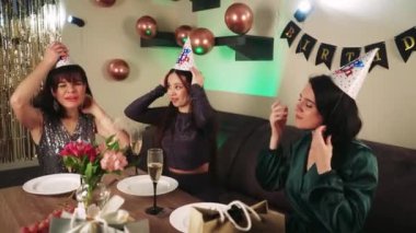 Doğum günü partisinde üç kadın, bir tabağa pizza koyup, evde doğum günü kutluyorlar. Parlak süslemeler ve balonlar