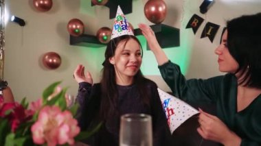 Doğum günü partisinde kutlama için şapka takan bir grup kadın. Masanın yanında renkli paketlerin içinde yıldönümü hediyeleri var.