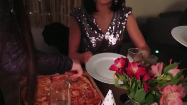 Yakın arkadaşlar pizza ve şekerlemeleri beyaz tabağa koymaya yardım eder. Mutlu bir doğum gününü dekorasyon ve hediyelerle kutlarlar. Arka planda, evde doğum günü için dekor var.